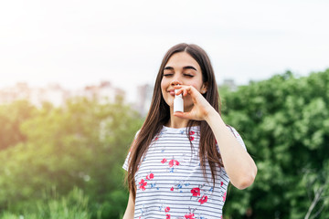 Young woman using nose spray for her pollen and grass allergies (Allergy relief) Flowering trees in...