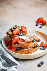 Traditional French toasts with blueberries, strawberries and powdered sugar on white plate.