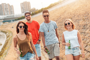 Group of cheerful friends walking through the city by the river talking and having fun.