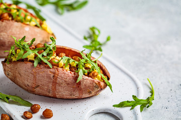 Baked sweet potato stuffed with fried chickpeas and vegan cheese on white background. Healthy vegetarian food concept.