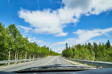 View from car window on the road and landscape with forest, tees, and blue sky with clouds....
