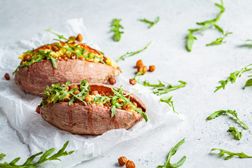 Baked sweet potato stuffed with fried chickpeas and vegan cheese on white background. Healthy vegetarian food concept.
