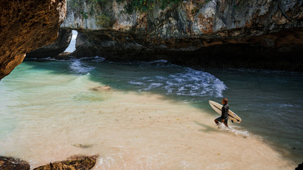 Surfer entering water in Suluban surfing spot. Bali, Indonesia. On vacation during a sunny day,...