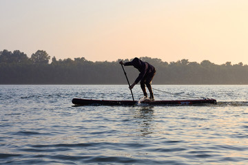 SUP silhouette of teenager standing with a paddle on the surfboard at sunset. Stand up paddle...