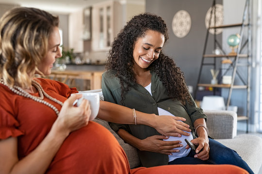 Friend Feeling Baby Bump Of Mixed Race Pregnant Woman