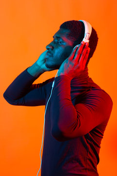 Young african-american man's listening to music in headphones in neon light. Male portrait. Concept of human emotions, facial expression, holidays or weekend, hobby,
