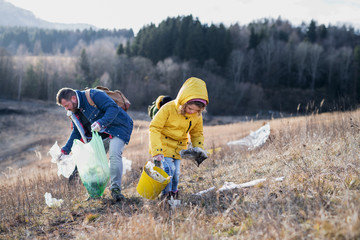 Small child with activists picking up litter in nature, environmental pollution concept.