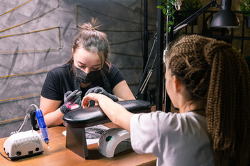 Female master uses an electric machine to remove the nail polish during manicure in the salon. Close-up hardware manicure. Concept of hand care. Female manicurist cleaning of nails by a milling cutter