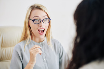 Shocked emotional young woman listening to exciting news her colleague telling her at meeting