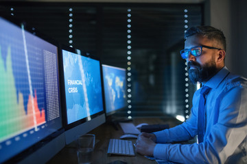 Businessman with computer sitting at desk, working late. Financial crisis concept.