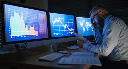 Frustrated businessman with computer sitting at desk, working late. Financial crisis concept.