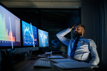 Frustrated businessman with computer sitting at desk, working late. Financial crisis concept.