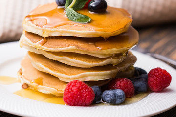 Pile of pancakes with blueberries and raspberries and maple syrup for breakfast on wooden table.