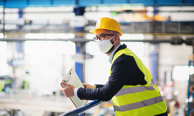 Technician or engineer with protective mask and helmet standing in industrial factory.
