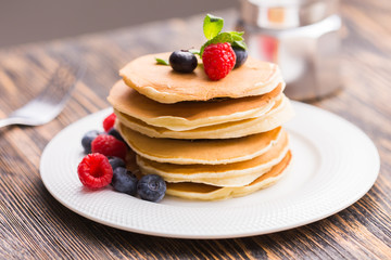 Pancakes with blueberries and raspberry on wooden background. Breakfast and traditional meal.