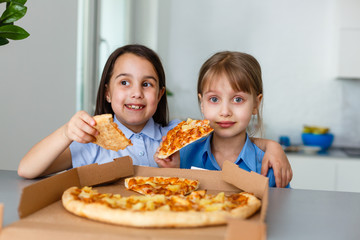 Two happy little child girl friends eating pizza slices.