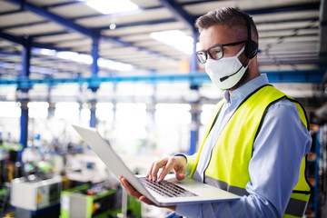 Technician or engineer with protective mask and laptop working in industrial factory.