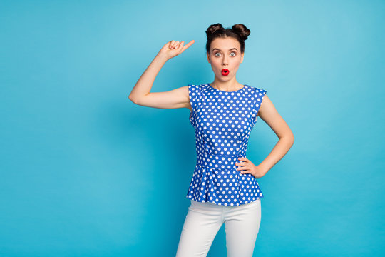 Photo of beautiful pretty lady indicating finger head cute hairstyle two buns not sure about hair style open mouth wear dotted blouse shirt white pants isolated blue color background