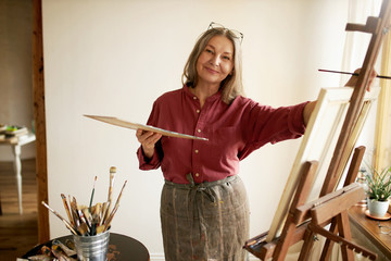 Creativity, inspiration, art and painting concept. Portrait of positive talented middle aged female...