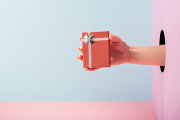 Woman's hand holding a gift box on blue and pink background