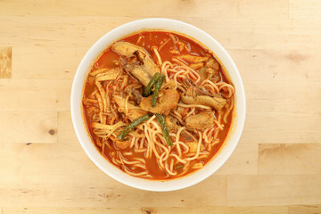 Malaysian curry yellow mee noodle with roasted chicken slice in white bowl on wooden background