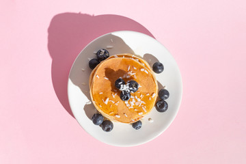 Pancakes with blueberries on a pink background with tough shadows. Top view
