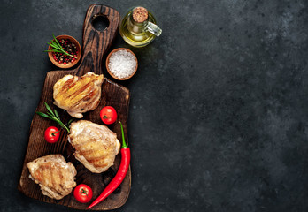 Obraz na płótnie Canvas Skinless grilled chicken thighs with spices on a cutting board on a stone background with copy space for your text