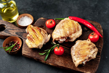 
Skinless grilled chicken thighs with spices on a cutting board on a stone background