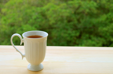 One cup of hot tea isolated on outdoor table with blurry green foliage in background	