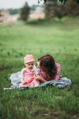 Young beautiful mother with small child have rest in the park on the lawn on warm day in pink clothes under the open sky