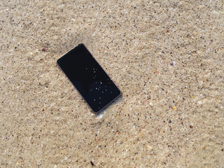 Mobile smart phone on the sandy beach with soft waves of sea background.  Internet of things concept.