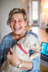 Senior woman with pet dog and laptop working in home office.