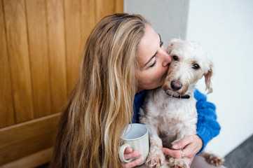 Mature woman relaxing outdoors by front door at home with coffee and pet dog.