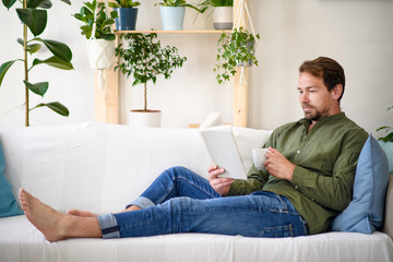Man sitting on sofa and reading book at home, lockdown concept.