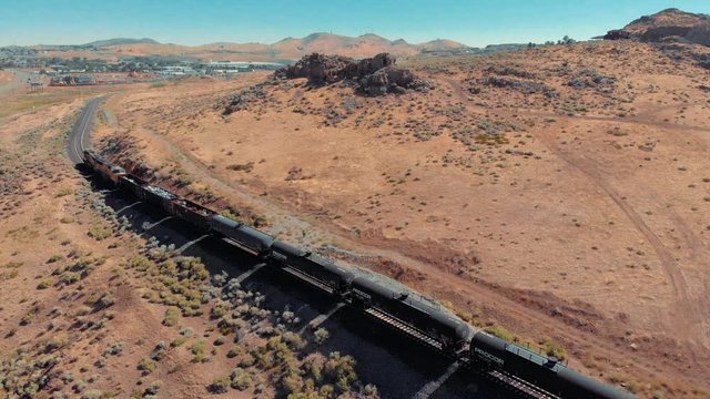 Drone footage of freight train heading through desert mountains towards a small desert town.  Gorgeous sunny day.
