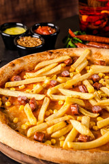 Italian Cuisine. Thin Oktoberfest pizza with french fries, hunting sausages and corn. Background image. copy space