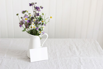Spring, summer still life. Enamel jug with wild flowers bouquet on linen table cloth. Daisies,...