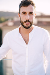 Stylish bearded guy in a white shirt and light trousers on a rooftop terrace in Florence, Italy