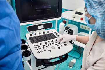 Doctor in white uniform with diagnostic equipment performs an ultrasound examination of leg veins of a female patient. Phlebologist working in modern clinic with Varicose Veins disease