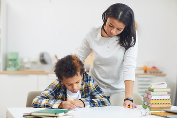 Portrait of young African mother helping teenage boy studying at home in minimal white interior, copy space