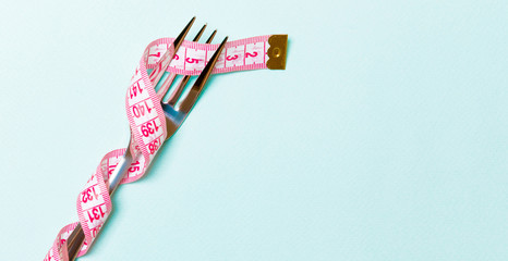 Fork wrapped in measuring tape on blue background. Top view of overeating concept