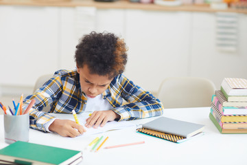 Portrait of African-American boy studying at home while sitting at desk in minimal interior, copy space