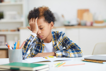 Portrait of tired African-American boy falling asleep at desk while doing homework, copy space