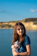 Fototapeta na wymiar Beautiful girl on the lake with a white kitten in her hands.