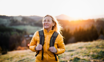 Attractive senior woman walking outdoors in nature at sunset, hiking. - Powered by Adobe