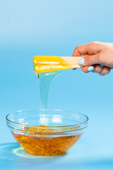 Liquid yellow wax or sugar paste for depilation drains from the stick on blue background. The concept of depilation, waxing, sugaring smooth skin without hair.