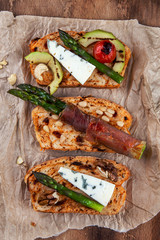 Homemade toasted bread served with green asparagus wrapped in bacon, cheese, avocado slices, grilled tomato cherry and nuts.