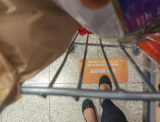 female feet next to a shopping cart with a sign on the floor written in portuguese (keep the distance 1.5 meters for a safe environment) rules during the coronavirus pandemic.