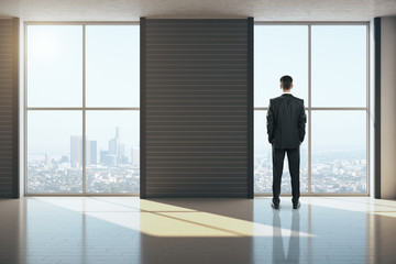 Fototapeta premium Businessman standing in clean gallery interior with city view.
