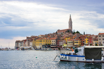 Rovinj, Croatia; 7/18/19: View of the typical croatian houses in the coastline of the old town of Rovinj, Croatia, with a boat on the right and the tower of the Church of St Euphemia on the top